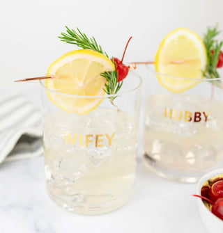 Wifey and Hubby rocks glasses half-filled with icy beverages are garnished with herbs, citrus, and cherries
