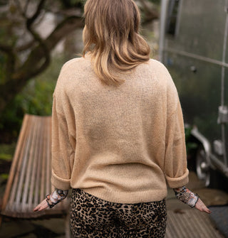Model facing away from the camera wears a tan-colored long-sleeved sweater with leopard print pants