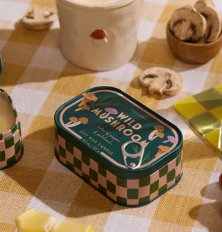 Wild Mushroom candle tin on a yellow gingham tablecloth with sliced mushrooms and other items