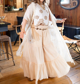 Model wears a long white kimono with subtle floral embroidery and fringe paired with a floral embroidered crop top and tiered wide leg pants
