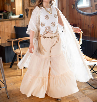 Model wears a long white kimono with subtle floral embroidery and fringe paired with a floral embroidered crop top and tiered wide leg pants