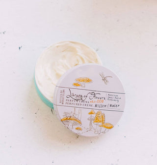Opened round container of Library of Flowers Willow & Water Parfum Crema features delicate, monochromatic illustrations of yellow-capped mushrooms and reveals creamy, white product inside