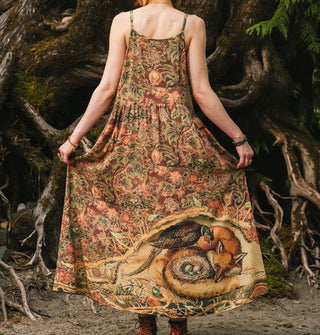 Model wears a brown sleeveless floral printed dress with illustration of a fox, pheasant, and nest of eggs at the bottom of its full-length skirt