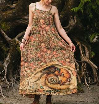 Model wears a floral printed sleeveless dress with illustration of a pheasant and fox with next of eggs on the bottom of the skirt